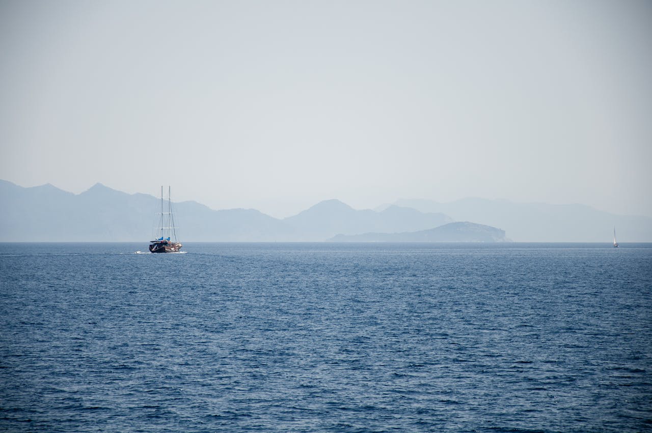 Home A sailboat gliding on the serene Mediterranean Sea with distant mountains near Marmaris, Turkey.