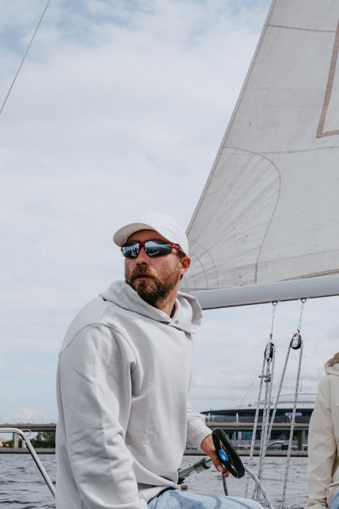Man wearing sunglasses navigating a yacht on a cloudy day, enjoying outdoor sailing.