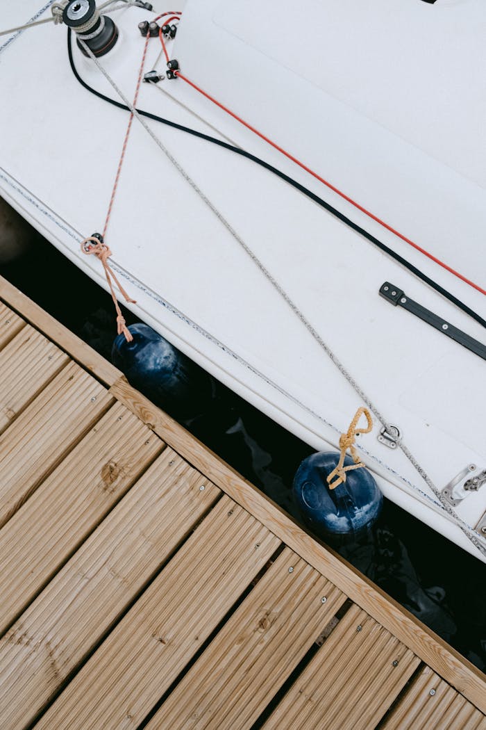 Home Detailed view of sailboat tied to a wooden dock, showcasing nautical ropes and equipment.